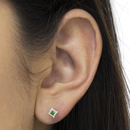 Close-up side view of an ear wearing a white metal stud earring with a square invisible setting and a green princess-shaped gemstone.