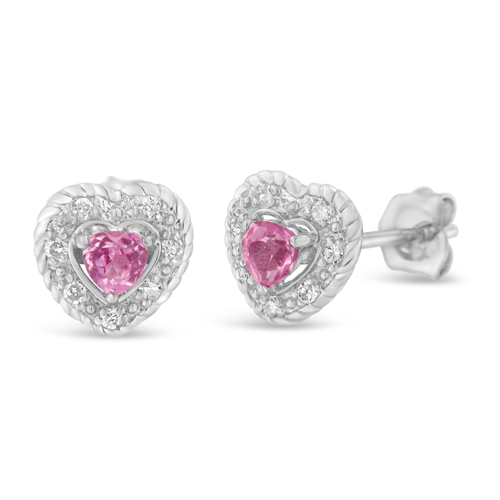 Close-up front angled view of white heart-shaped earrings with pink heart-shaped gemstones in the center surrounded by small round white gemstones in pave setting.