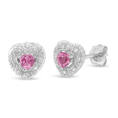 Close-up front angled view of white heart-shaped earrings with pink heart-shaped gemstones in the center surrounded by small round white gemstones in pave setting.
