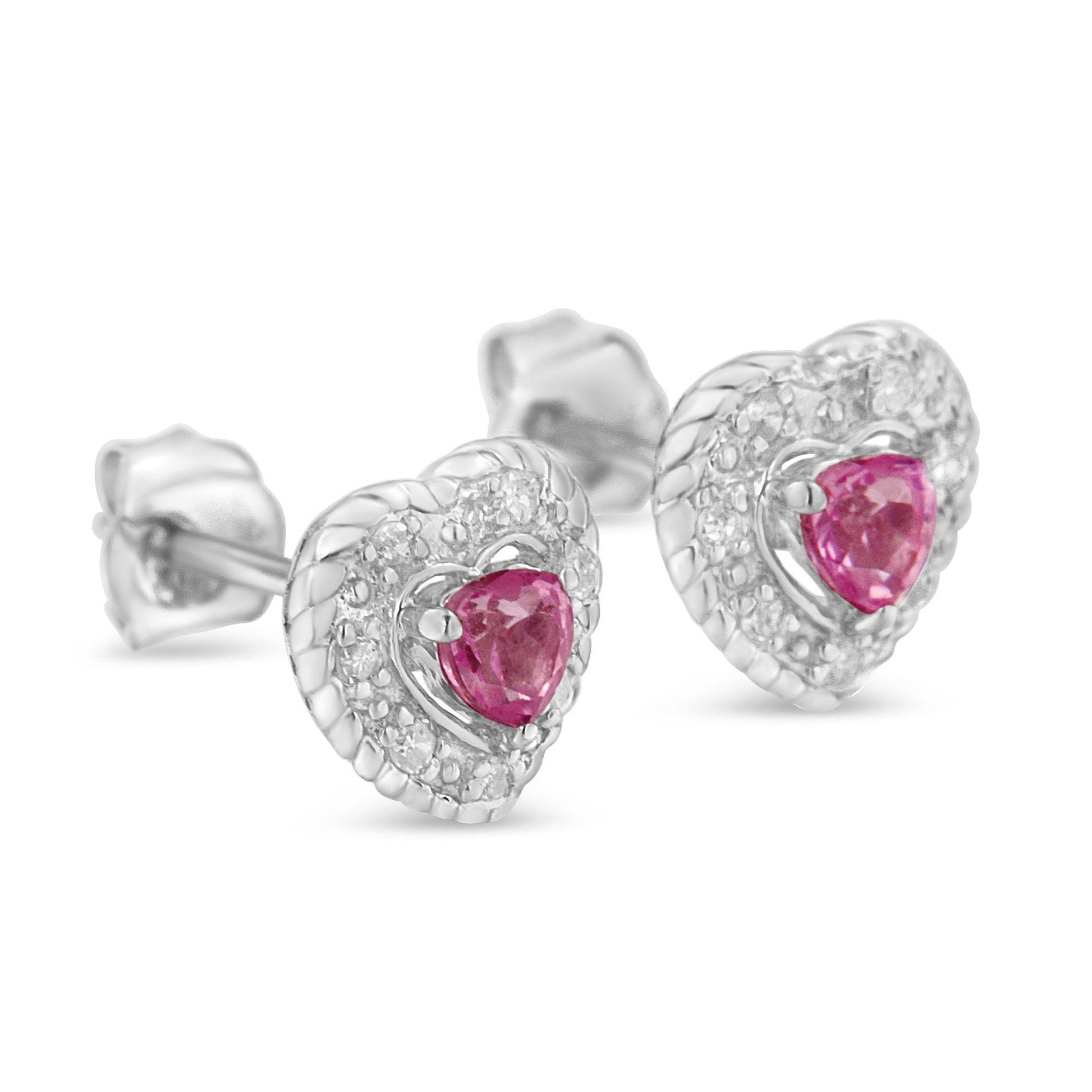Close-up side angle of a pair of white metal heart-shaped stud earrings featuring a pink heart-shaped gemstone at the center surrounded by small round white gemstones in a pave setting.