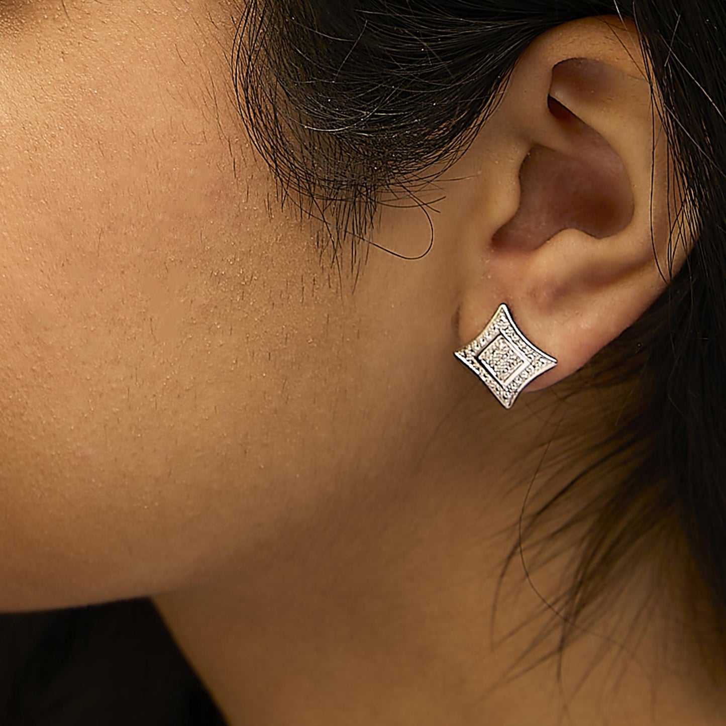 Close-up side view of a white metal earring with a geometric shape featuring round white gemstones in pave setting, worn on a model.