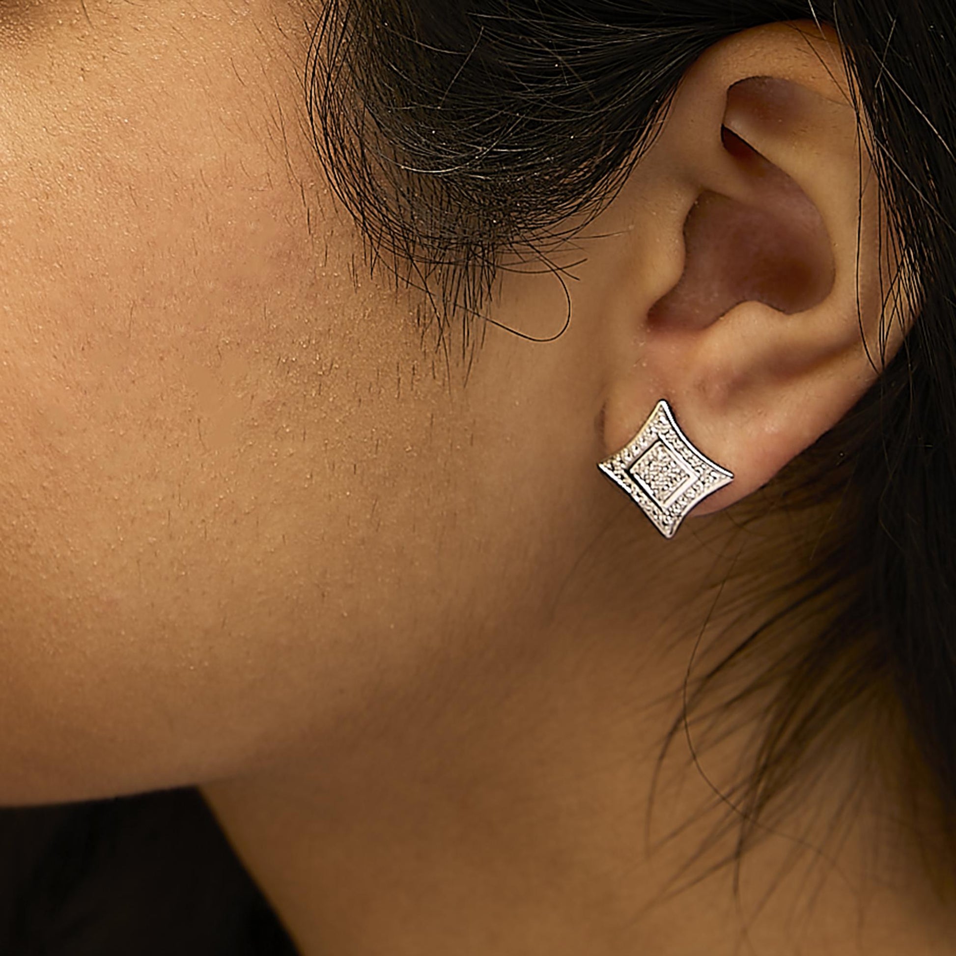 Close-up side view of a white metal earring with a geometric shape featuring round white gemstones in pave setting, worn on a model.