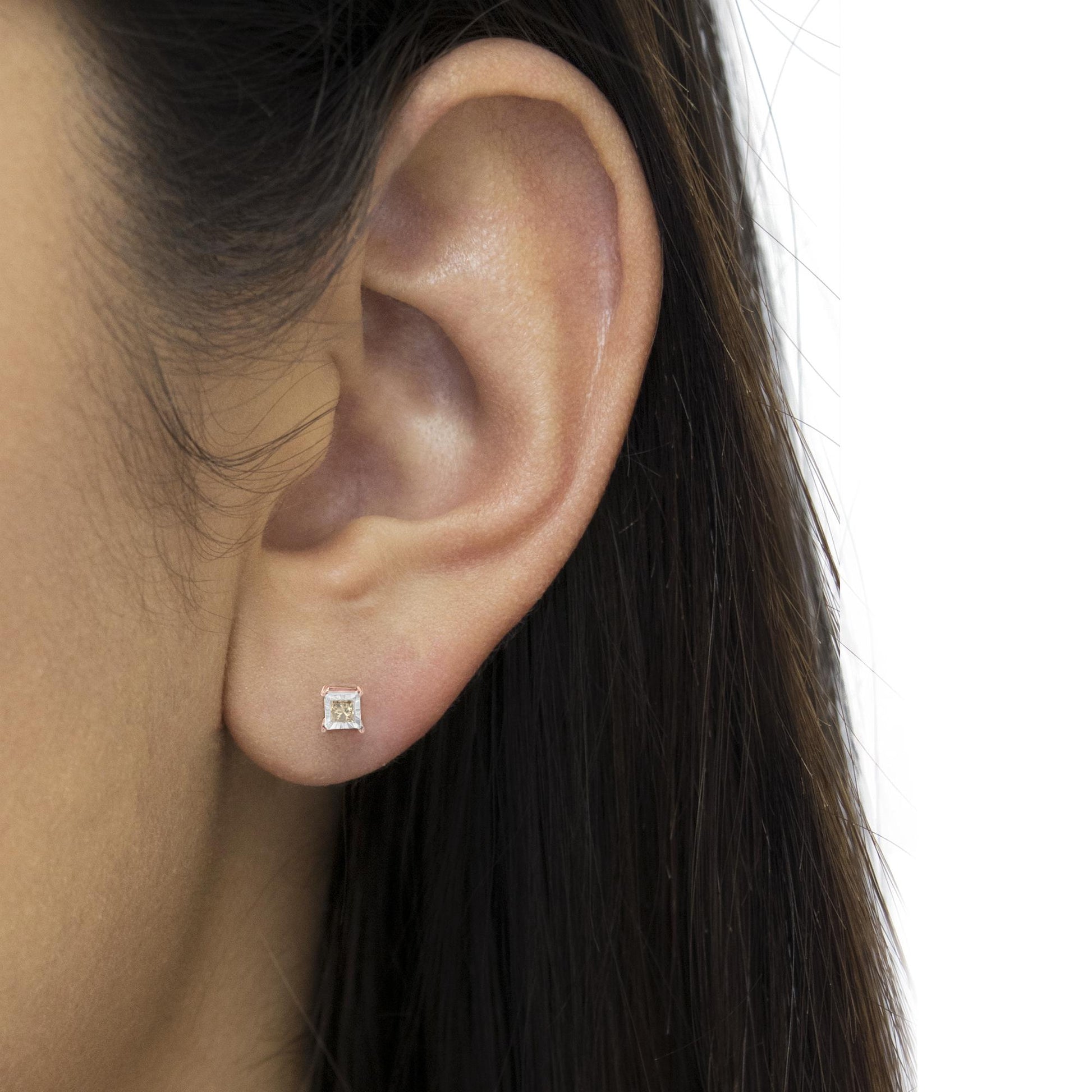 Close-up shot of a square-shaped stud earring with a brownish gemstone set in white and rose metal, worn on a model's ear.