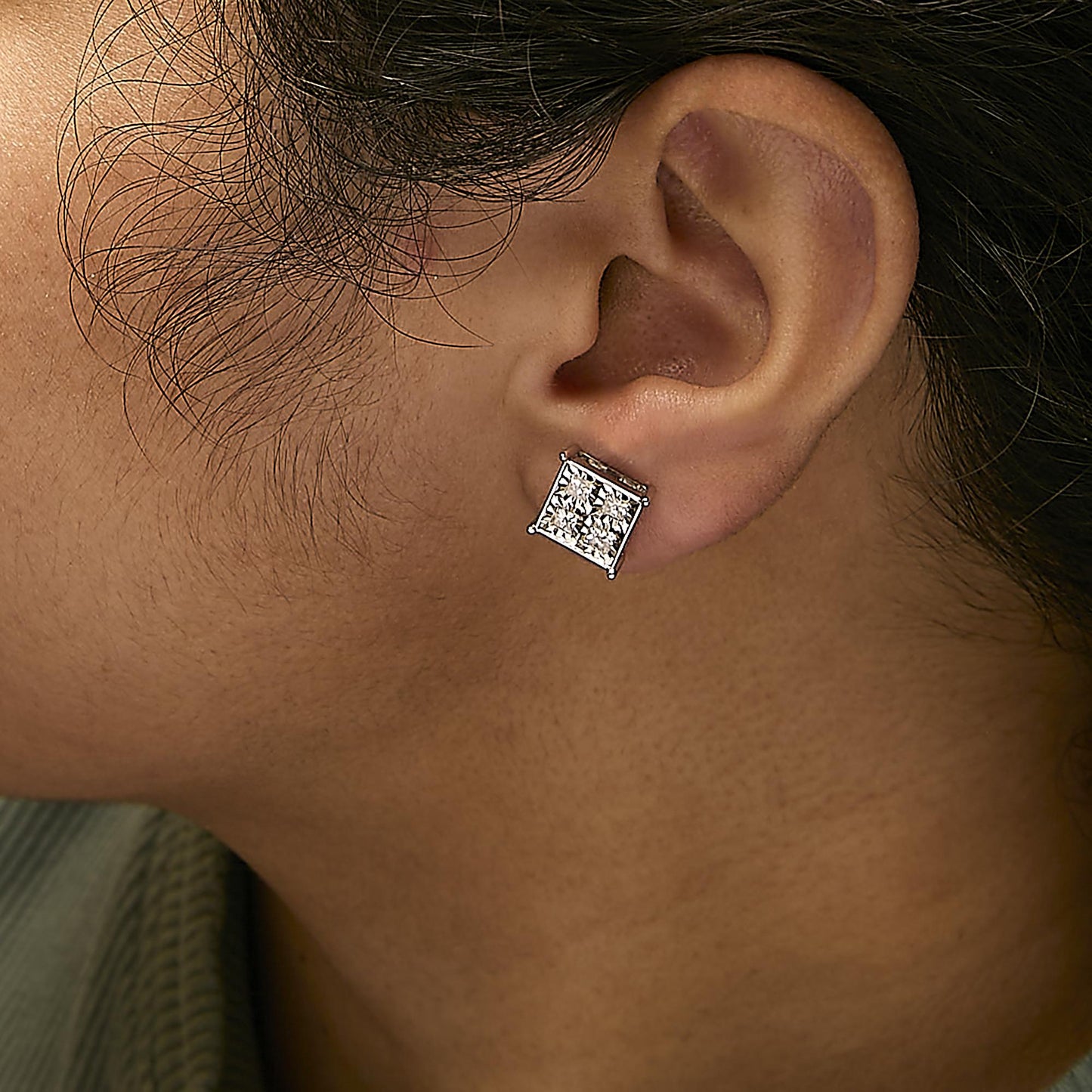 Close-up side view of a model wearing white metal square stud earrings with multiple white gemstones in an invisible setting.