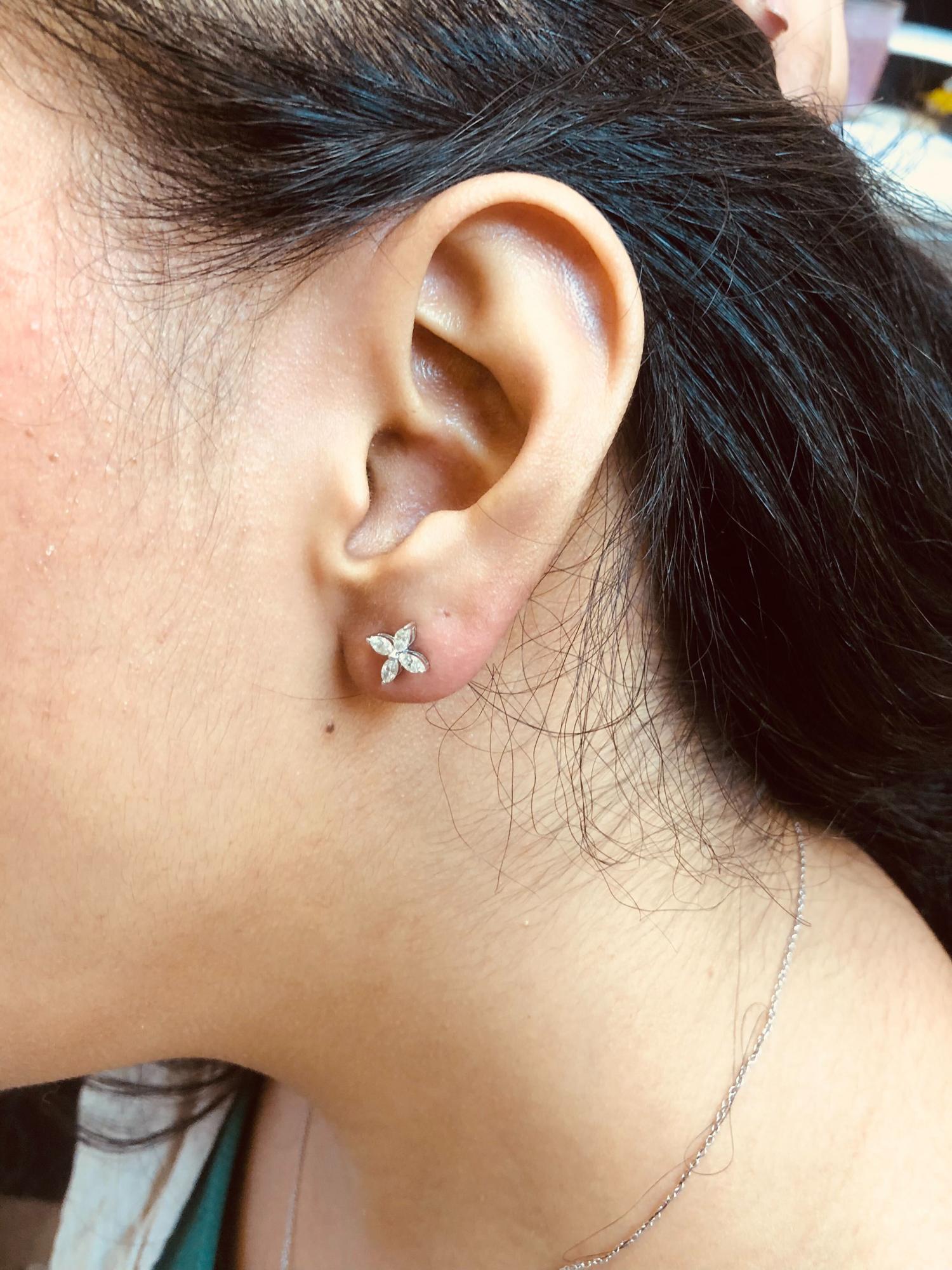 Close-up side view of a model wearing white metal stud earrings featuring a flower shape made of marquise-shaped white gemstones in a prong setting.