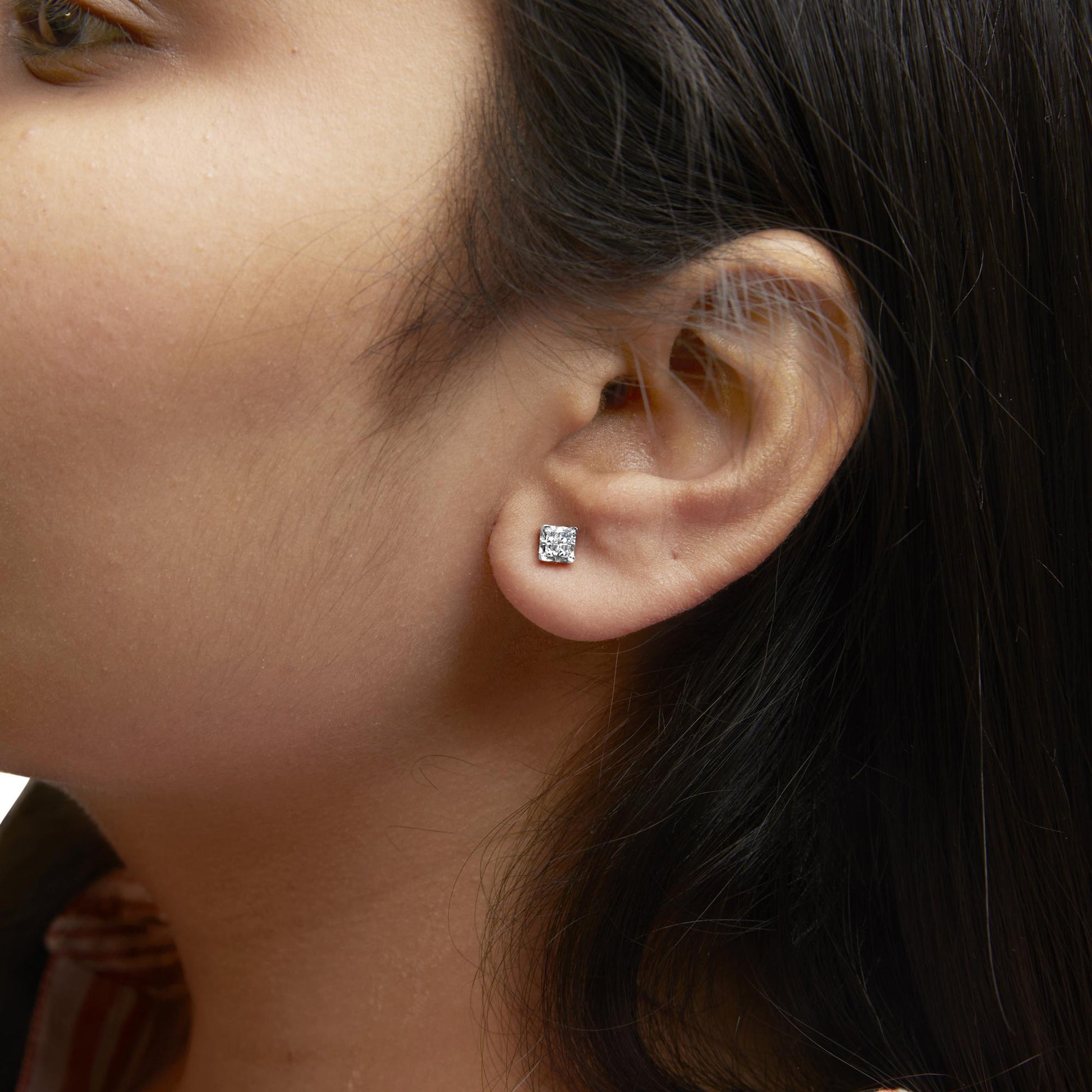 Close-up side angle of a model wearing yellow metal stud earrings with white princess-shaped gemstones in an invisible setting.