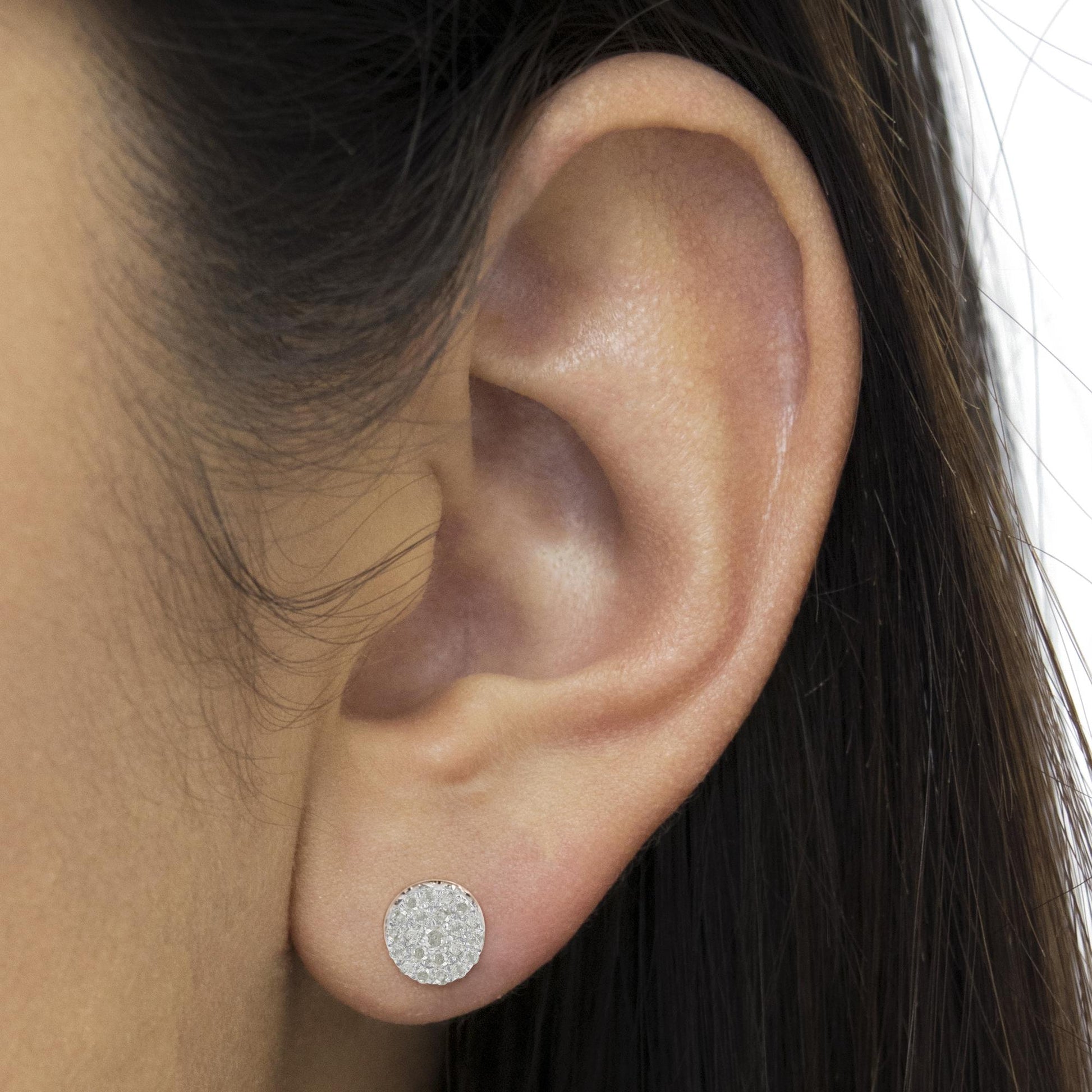 Close-up of a white metal round stud earring with pave-set white gemstones, worn on a model's ear.
