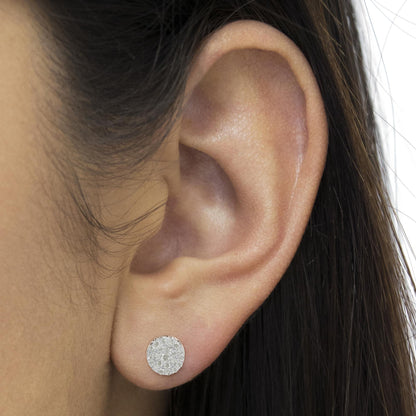 Close-up of a white metal round stud earring with pave-set white gemstones, worn on a model's ear.