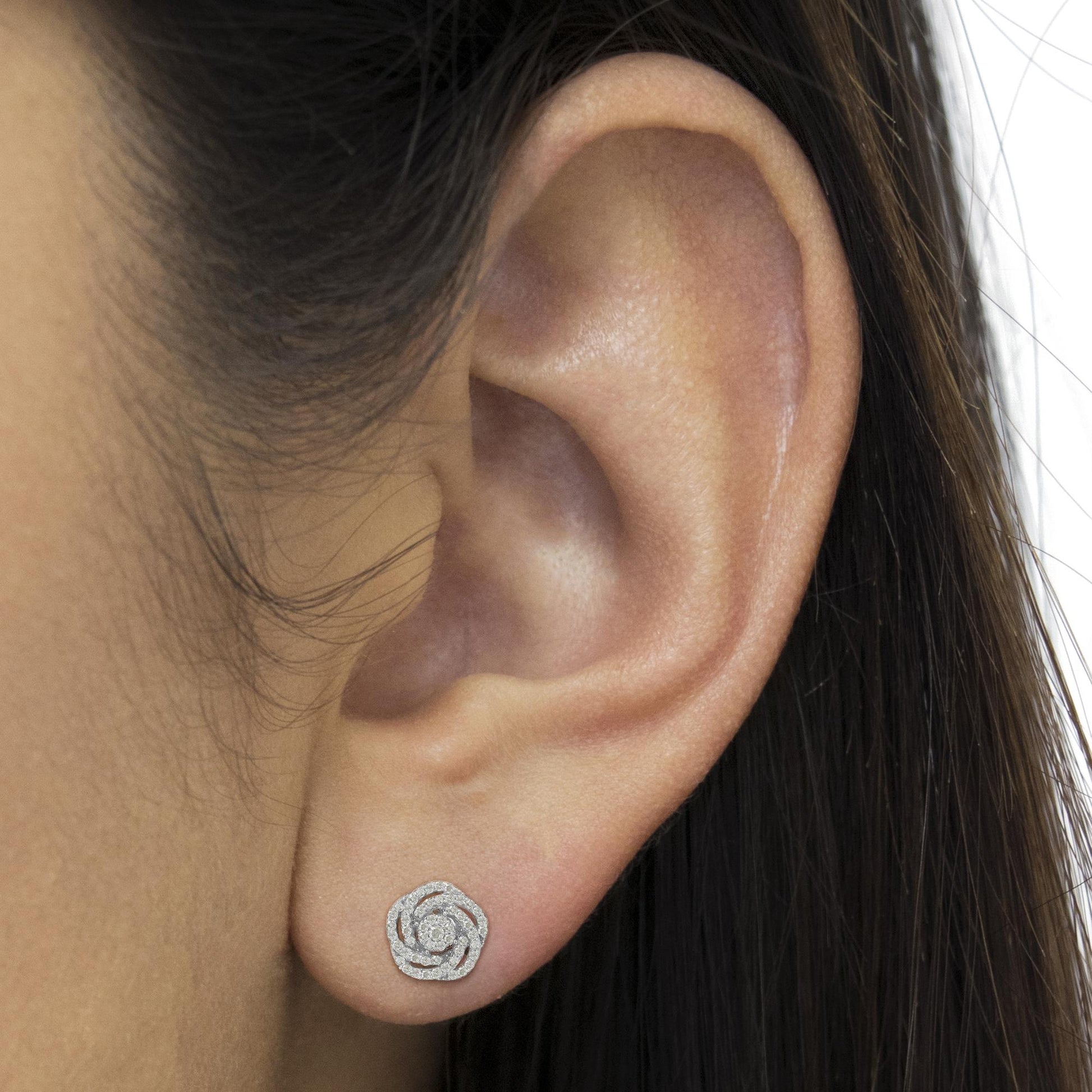 Close-up side view of a model's ear wearing a white metal earring with round white gemstones in a prong setting forming a floral swirl design.