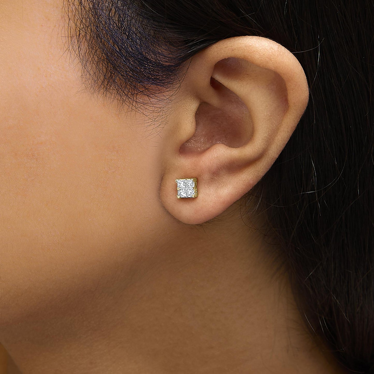 Close-up side view of a yellow metal earring with a cluster of white princess-shaped gemstones in an invisible setting, worn on a model's ear.