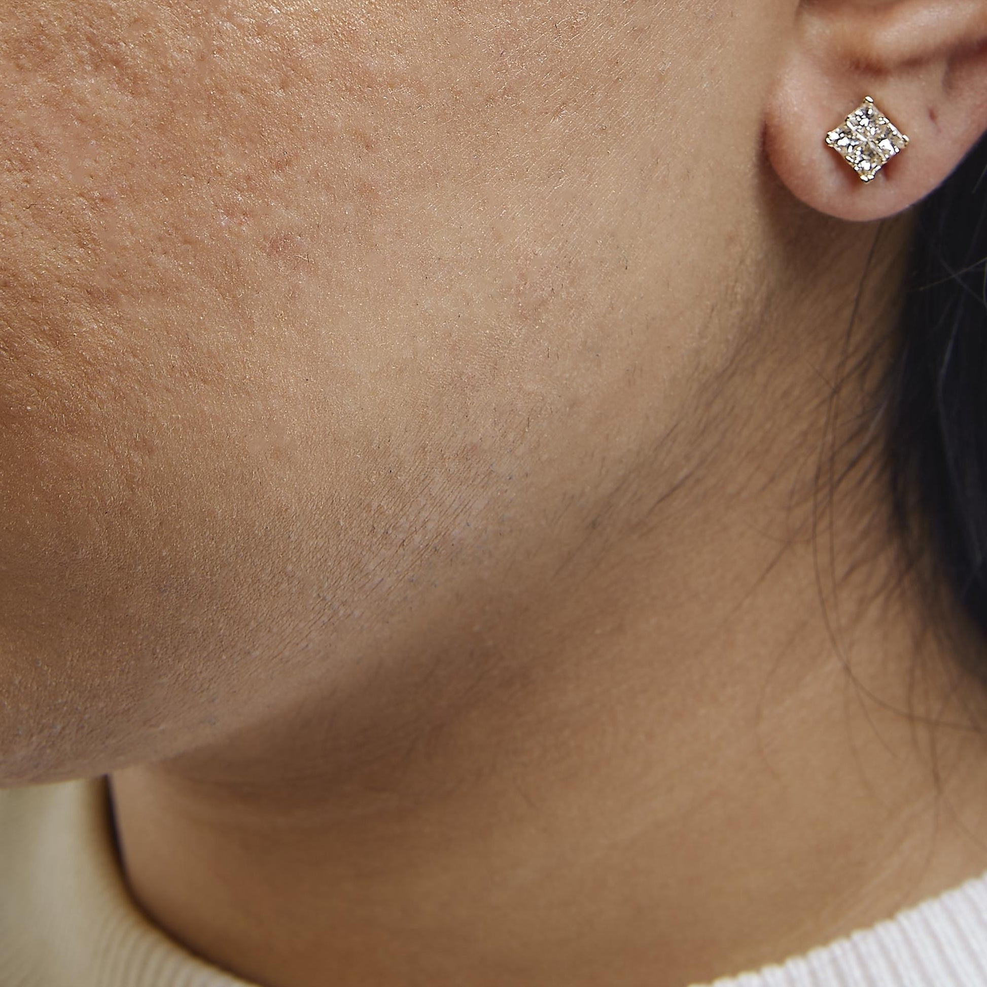 Close-up side angle of a yellow metal earring on a model's ear, featuring princess-shaped white gemstones in an invisible setting.