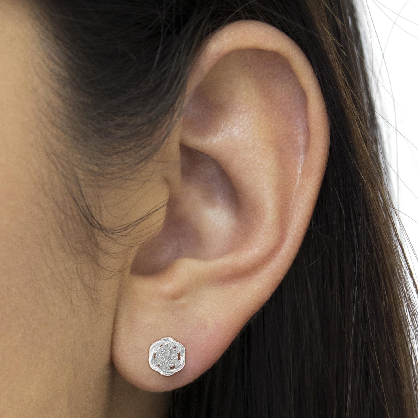 Close-up side view of a white metal flower-shaped stud earring with multiple round white gemstones set in the center, worn on a model's ear.