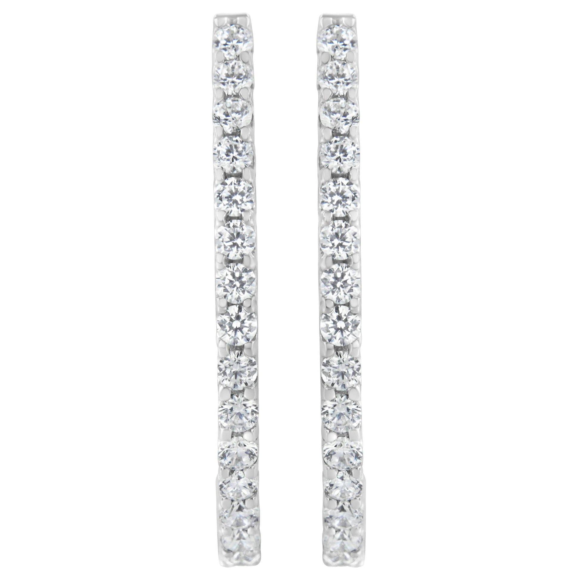 Front-facing shot of a pair of white metal earrings each set with a vertical line of round white gemstones in prong settings.