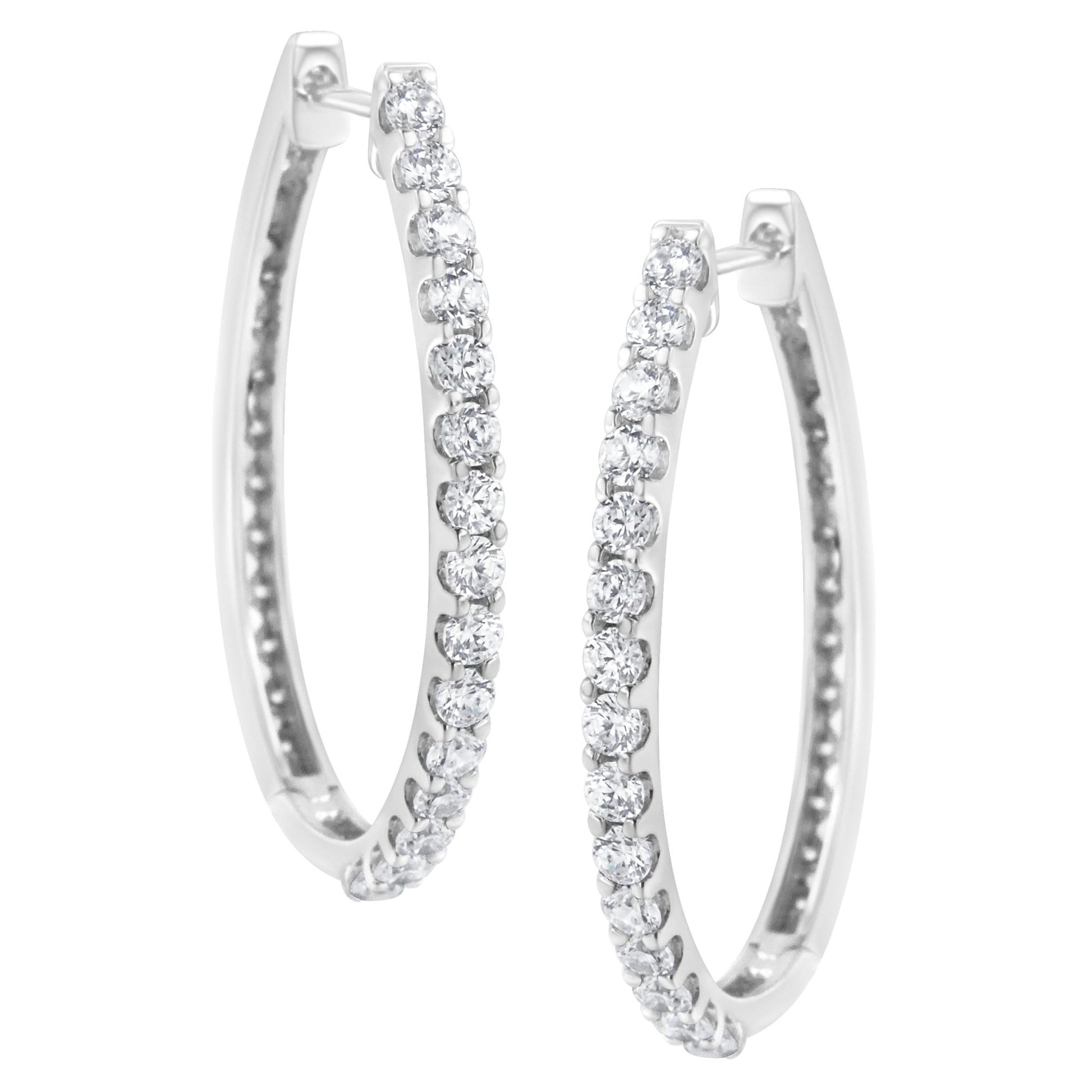 Front angled view of white metal hoop earrings set with round white gemstones in prong settings along the outer edge.