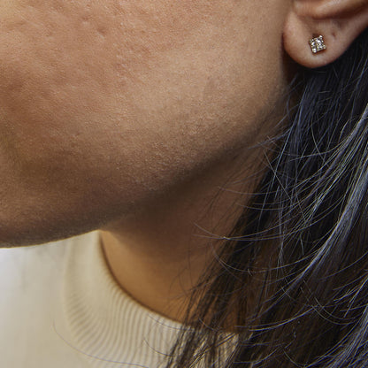Close-up side view of a model wearing a yellow metal stud earring with multiple small princess-shaped white gemstones in an invisible setting.
