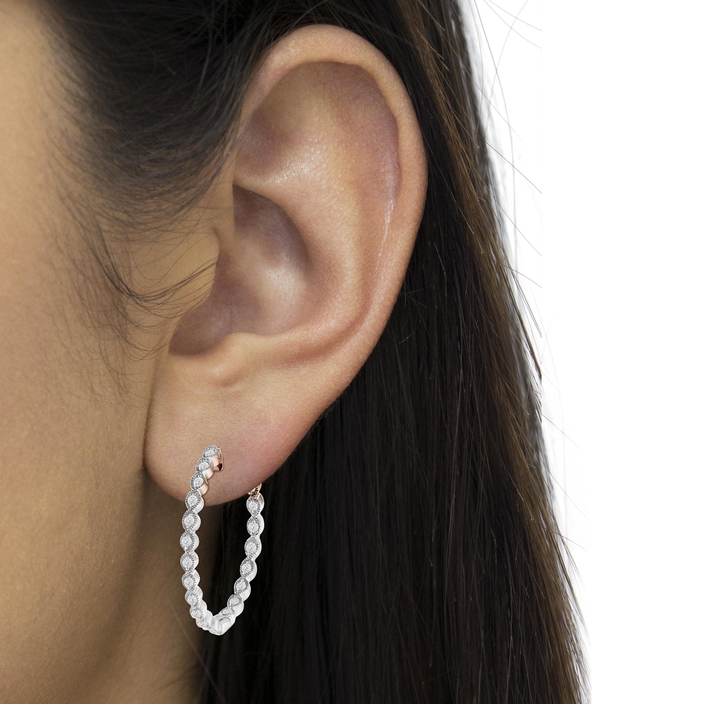 Close-up side angle of white metal hoop earrings with round white gemstones in prong settings, worn on a model.