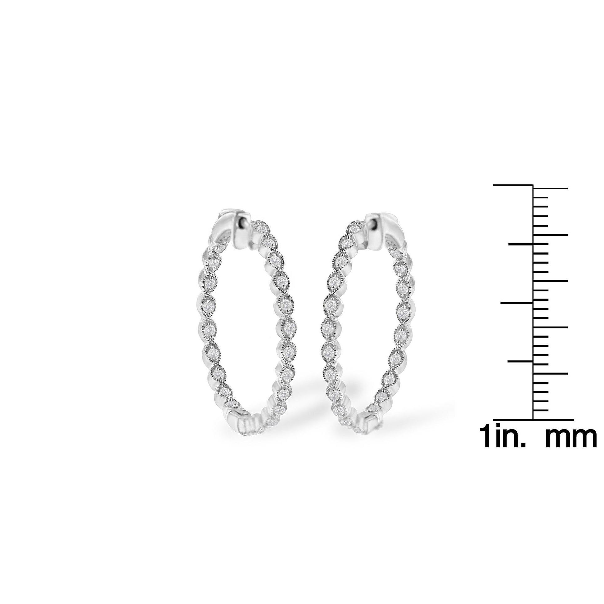 Pair of white metal hoop earrings embellished with round prong-set white gemstones, shown from a front angle, positioned next to a ruler for size reference.
