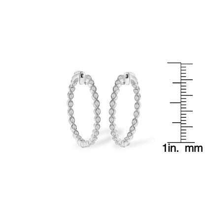 Pair of white metal hoop earrings embellished with round prong-set white gemstones, shown from a front angle, positioned next to a ruler for size reference.