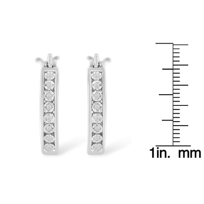 Front view of pair of white metal earrings with white round gemstones set in a vertical line, displayed next to a ruler for size reference.