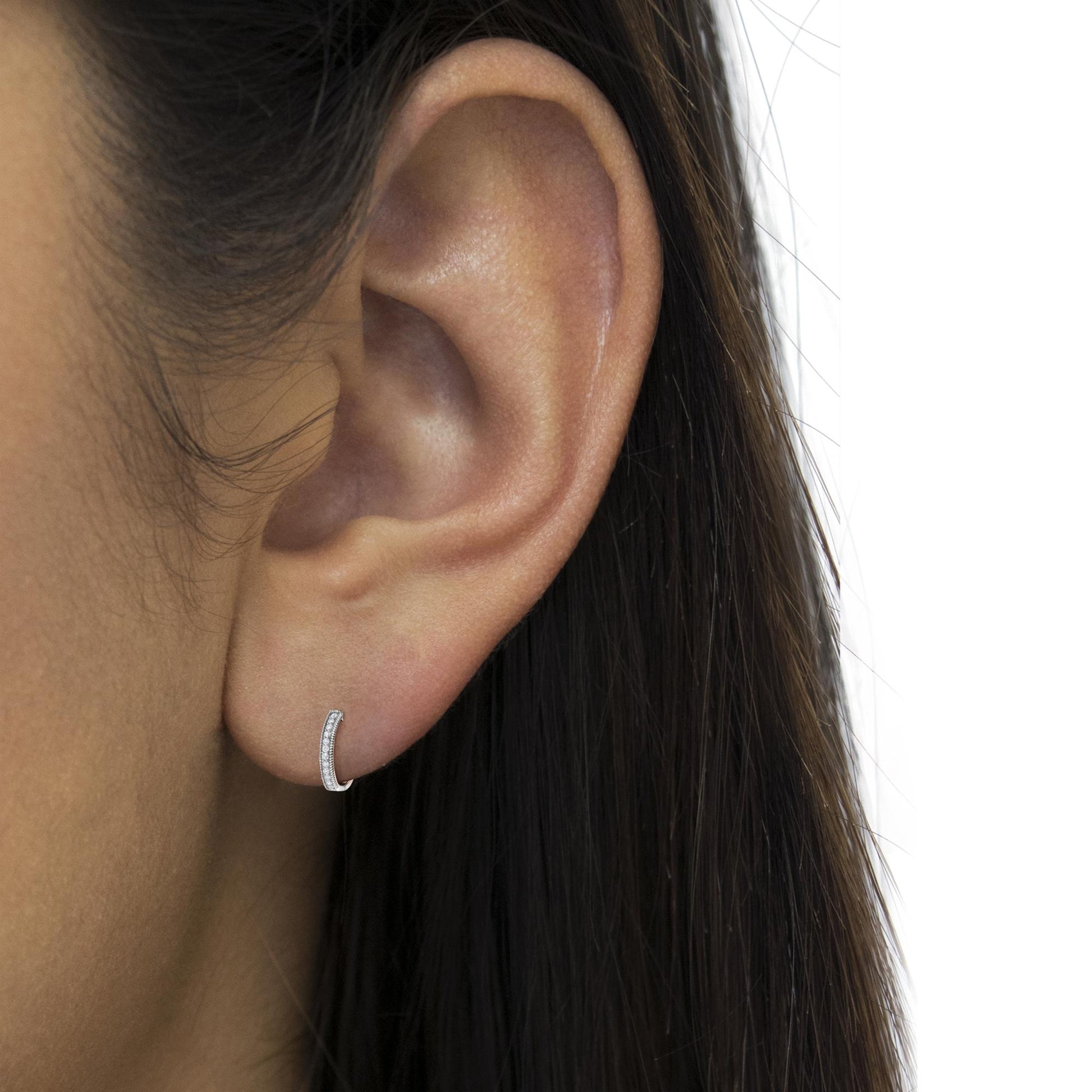 Close-up side view of a white metal small hoop earring with two rows of round white gemstones in prong settings, worn on a model.