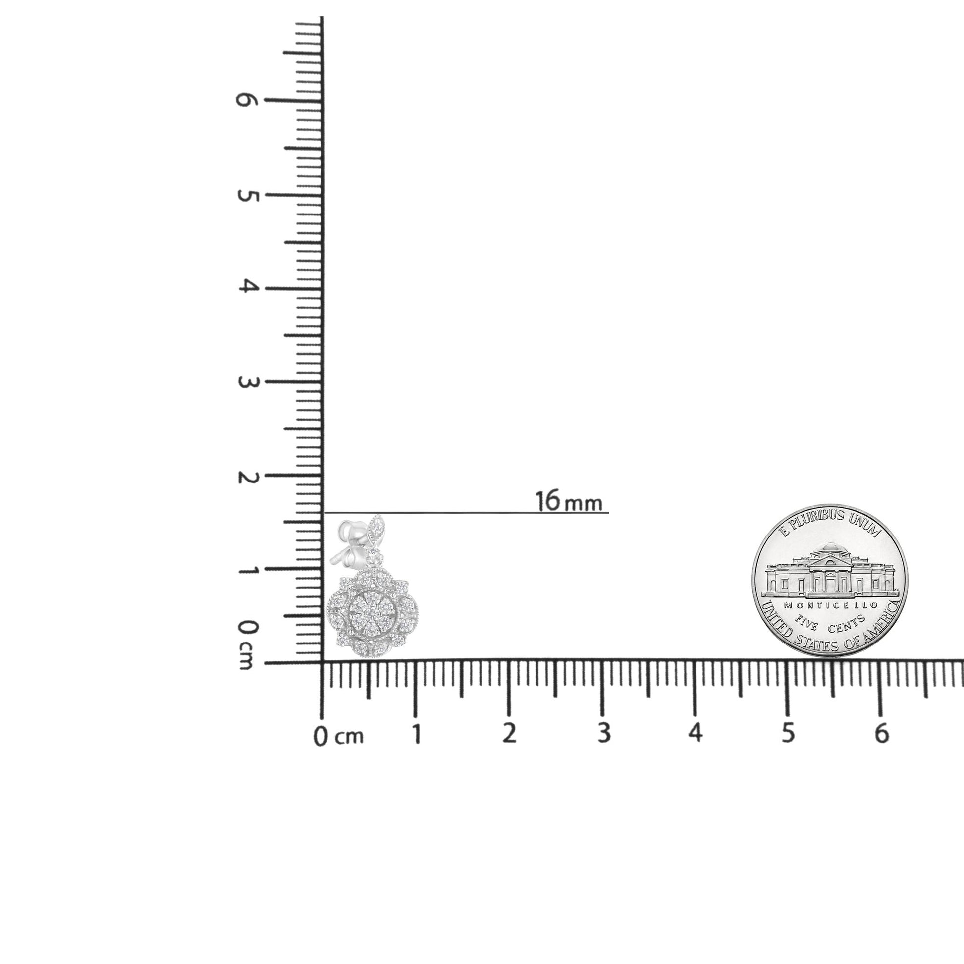 Close-up angled shot of white metal drop earrings with round white gemstones in prong settings, displayed on a ruler for size reference with a coin nearby.