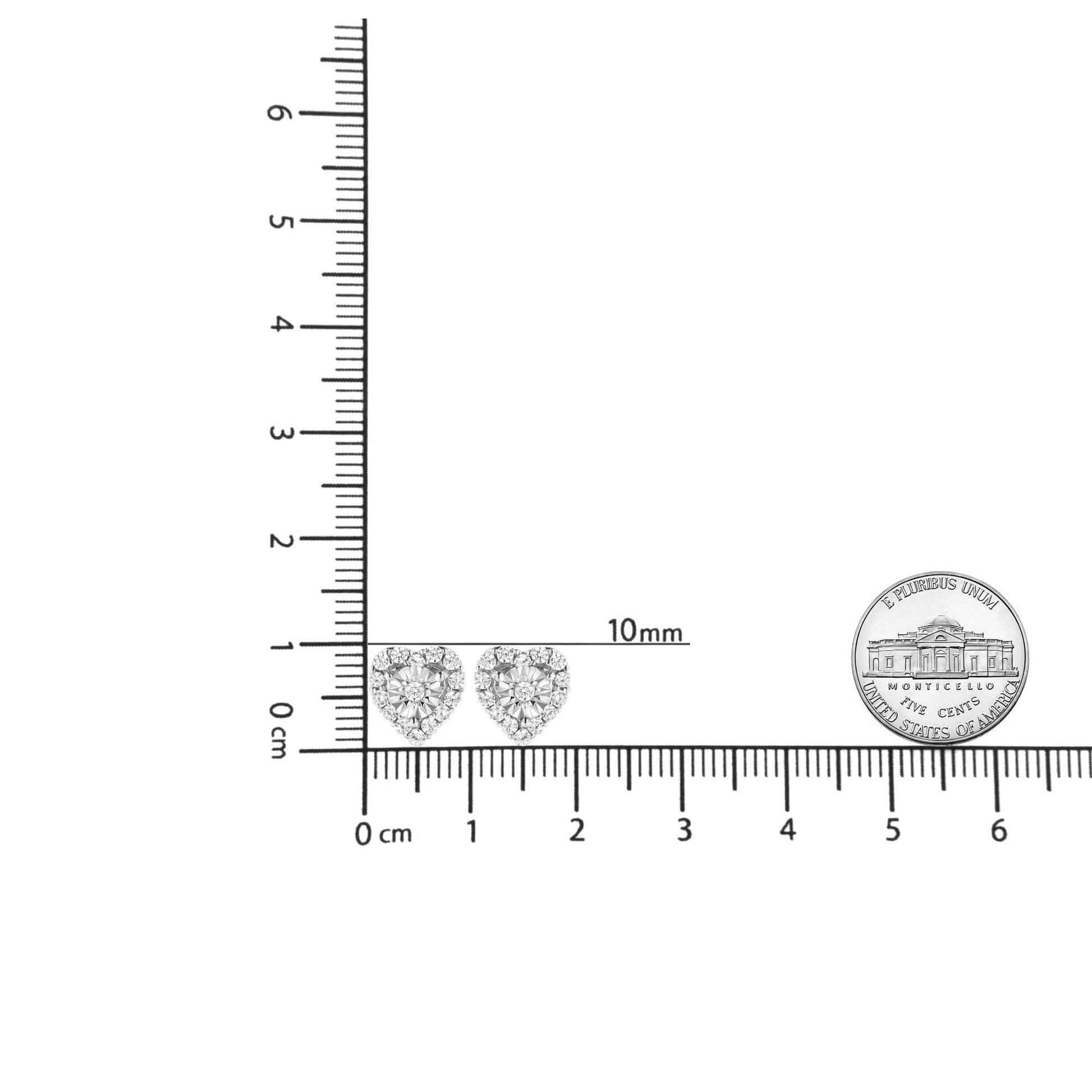 Pair of white heart-shaped earrings with round white gemstones in prong and miracle settings, shown from the front on a ruler for size reference.