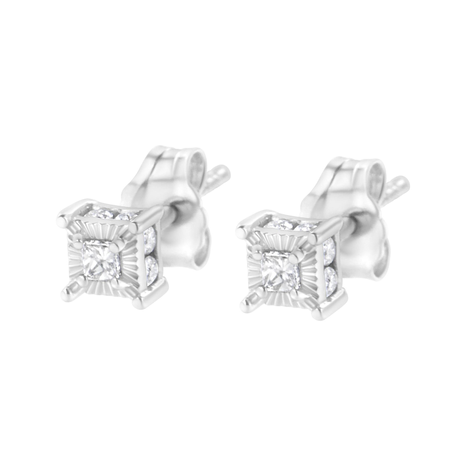 Pair of white metal stud earrings with princess shape white gemstones in prong settings at the center, surrounded by round shape white gemstones in channel settings, shown from a front angle.