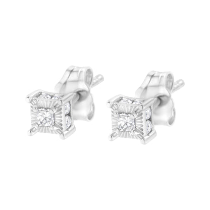 Pair of white metal stud earrings with princess shape white gemstones in prong settings at the center, surrounded by round shape white gemstones in channel settings, shown from a front angle.