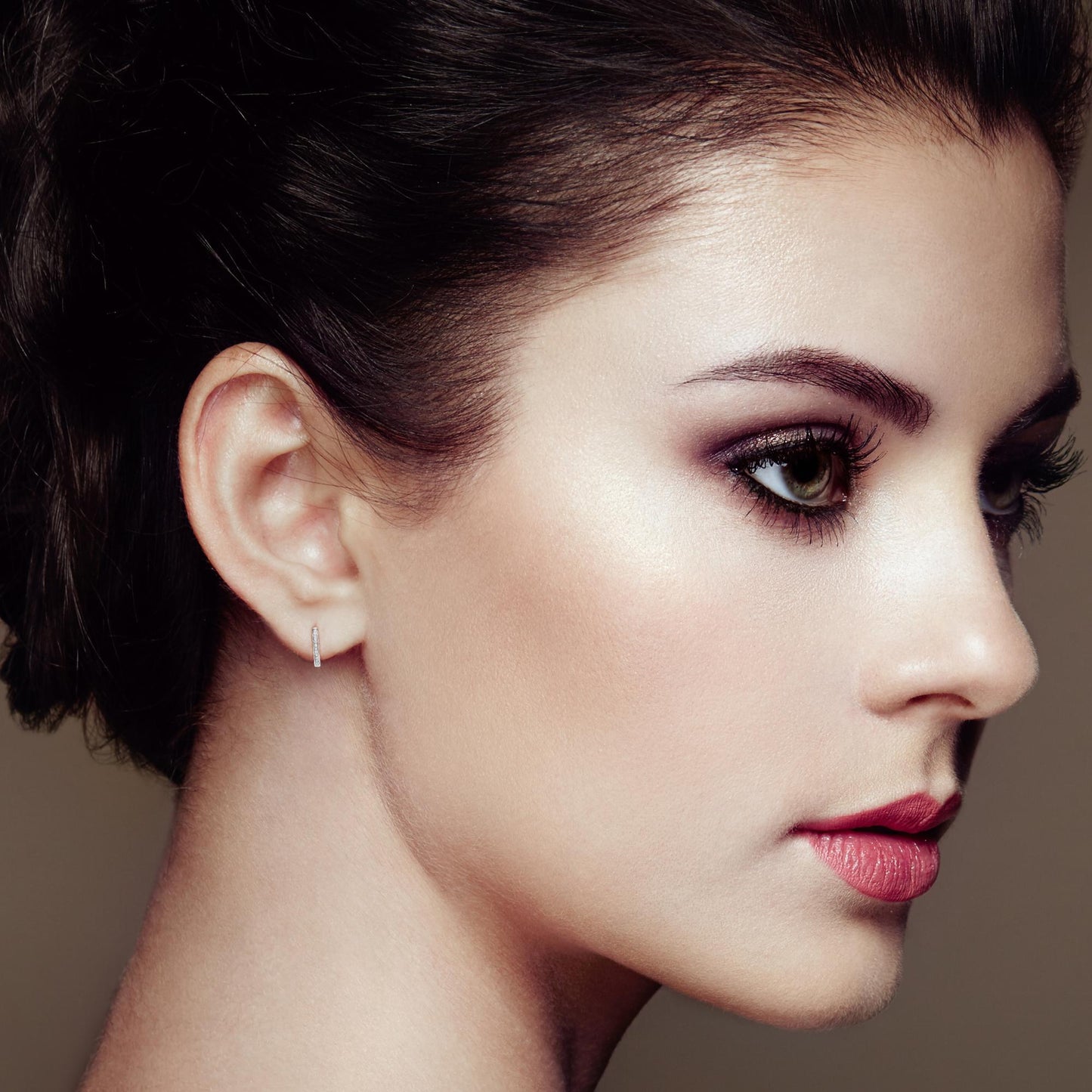 Close-up side profile of a model wearing small white metal earrings with round white gemstones in a pave setting.