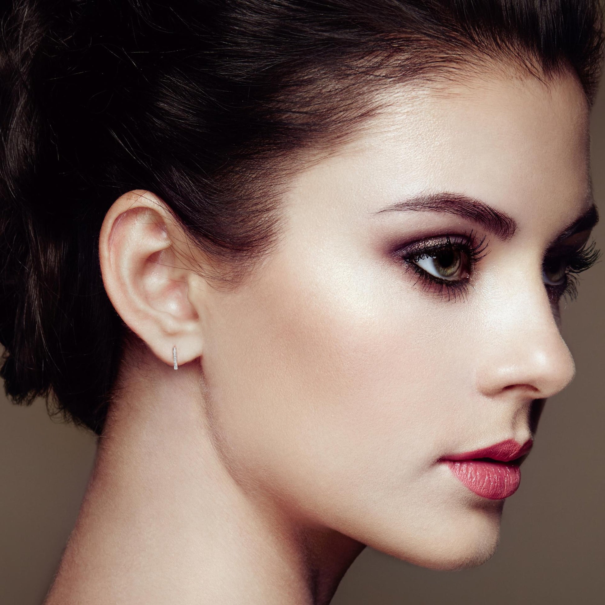 Close-up side profile of a model wearing small white metal earrings with round white gemstones in a pave setting.