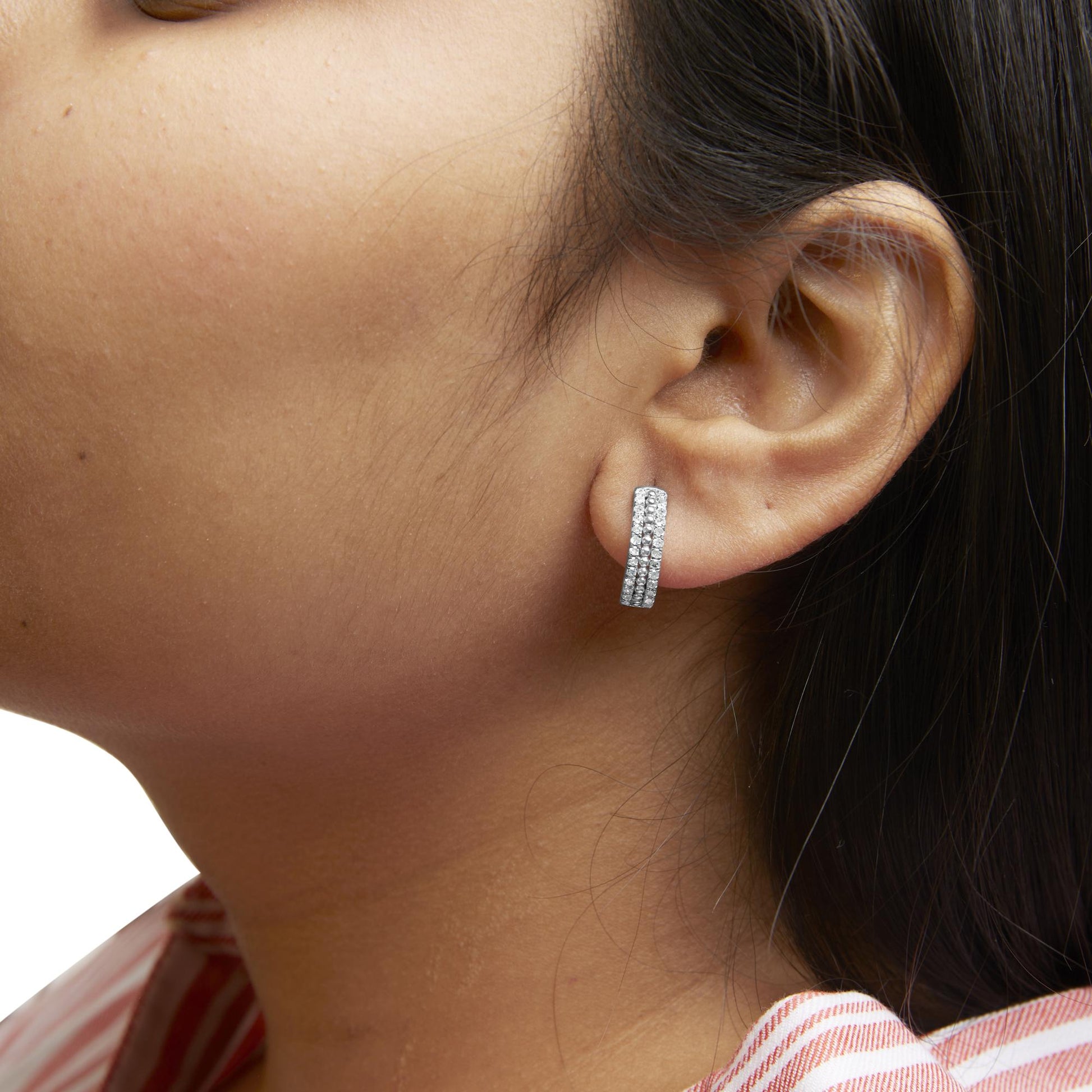 Close-up side view of a white metal earring with three rows of round white gemstones in pave setting, worn on a model's ear.