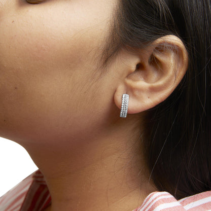 Close-up side view of a white metal earring with three rows of round white gemstones in pave setting, worn on a model's ear.