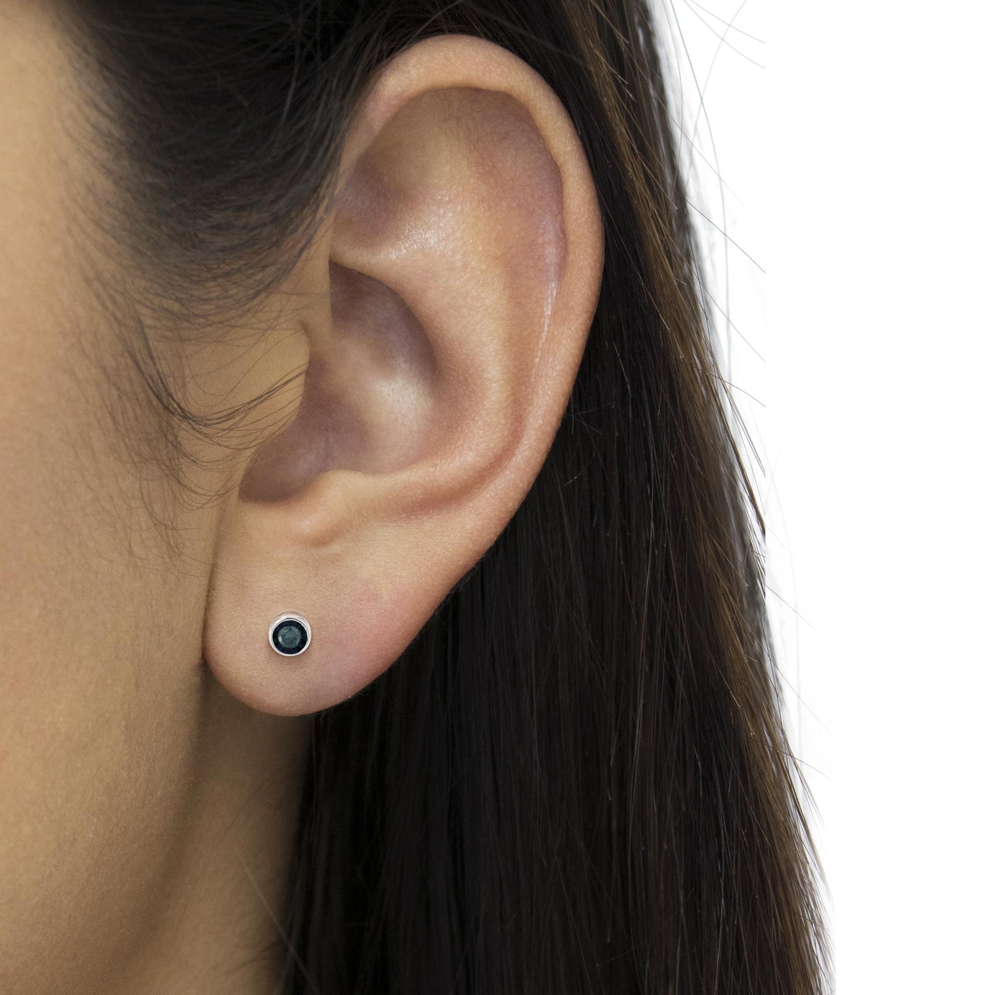 Close-up side view of a white metal stud earring with a round blue gemstone in miracle setting, worn on a model's ear.