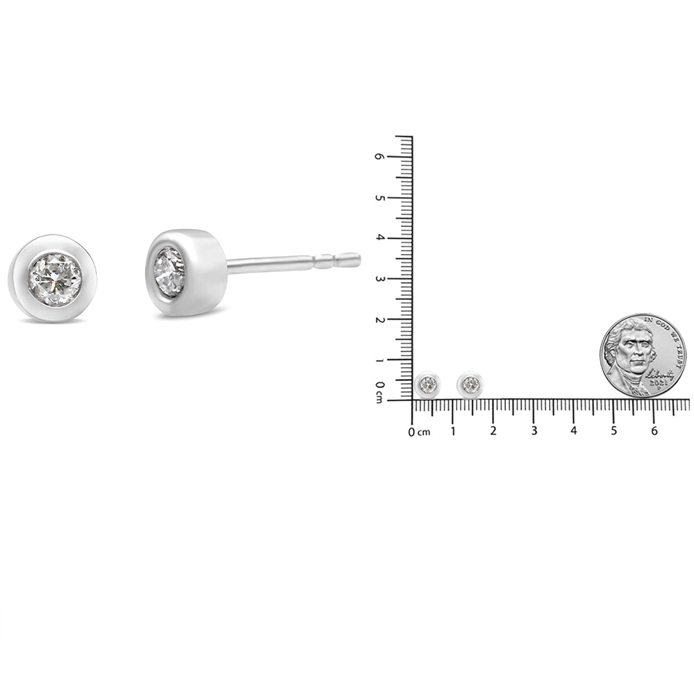 Close-up side and front view of white metal stud earrings with round bezel-set white gemstones, shown next to a ruler and coin for size reference.