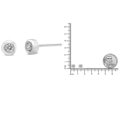 Close-up side and front view of white metal stud earrings with round bezel-set white gemstones, shown next to a ruler and coin for size reference.