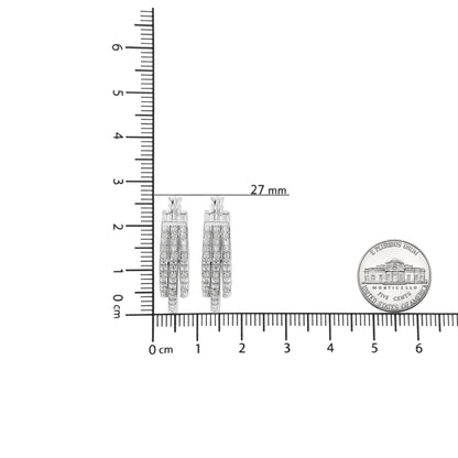 Front-facing image of white metal earrings with multiple rows of round white gemstones in pave setting, placed on a ruler for size reference.