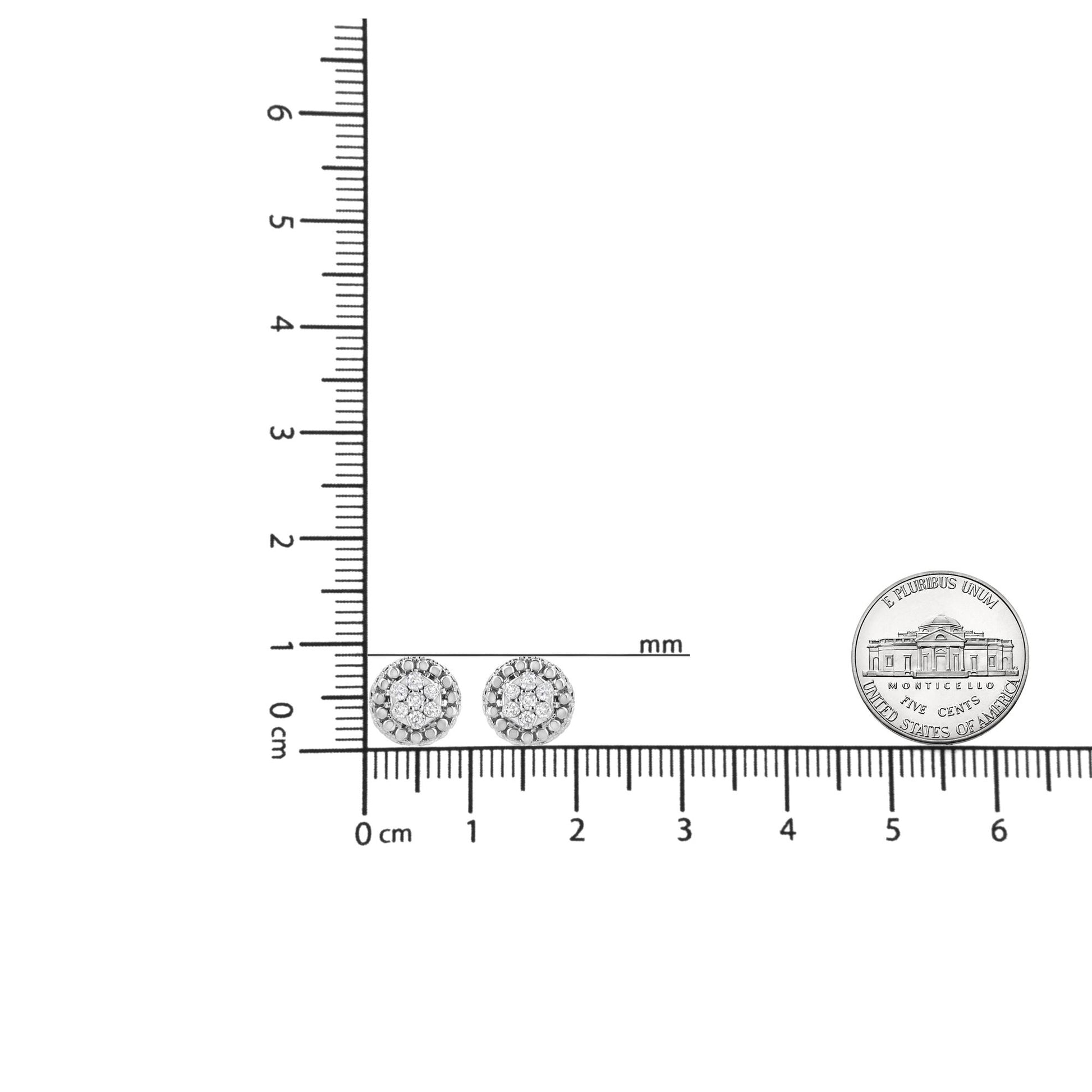 Pair of round white metal earrings with pave set white gemstones, shown from front on a ruler and coin for size reference.