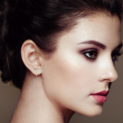Close-up side profile of a model wearing small yellow metal hoop earrings set with multiple white round gemstones, shot from the right side.
