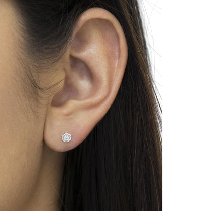 Close-up side view of a white metal stud earring with a round white gemstone in a bezel setting, worn on a model's ear.