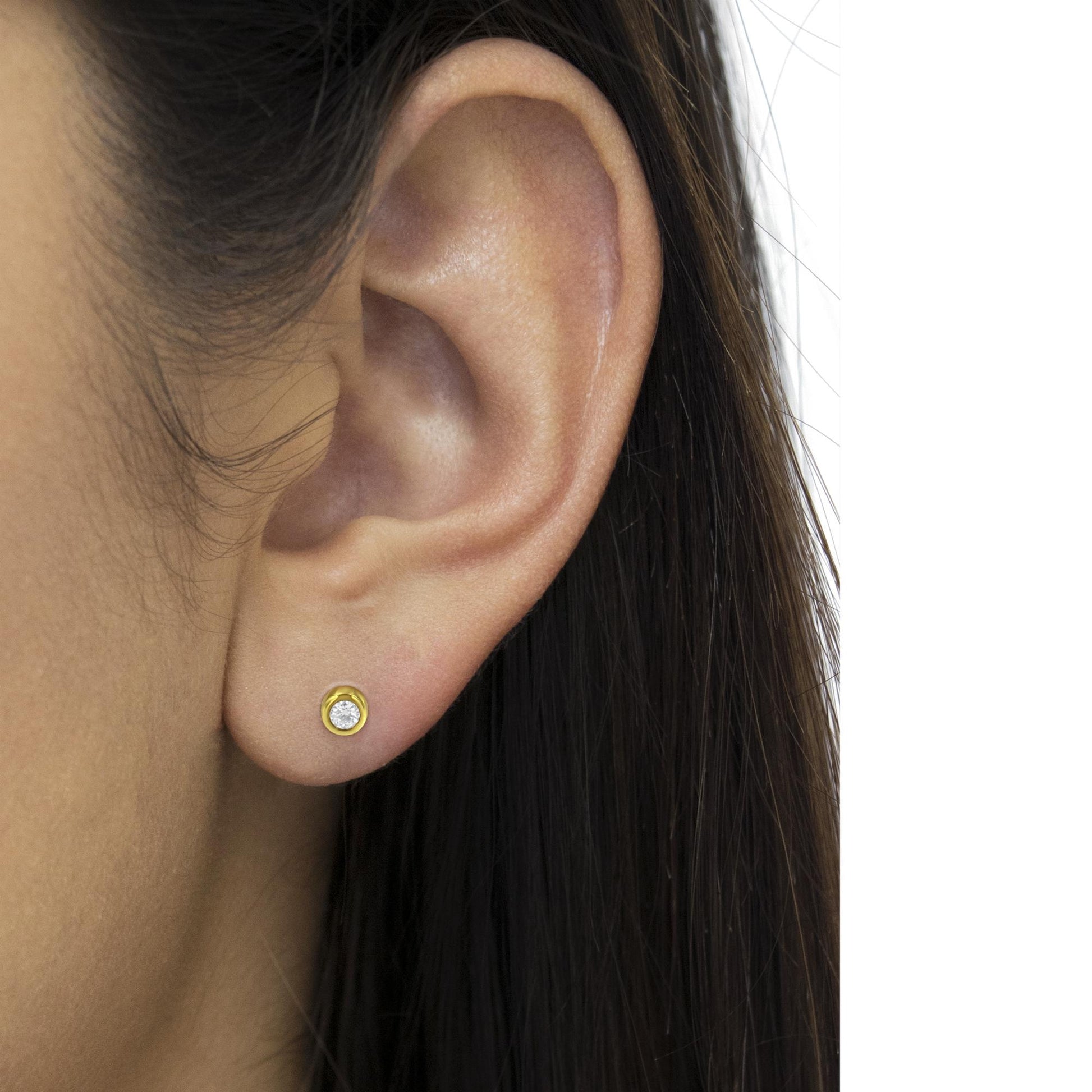 Close-up side view of a yellow metal stud earring with a round white gemstone in a bezel setting, worn on a model.