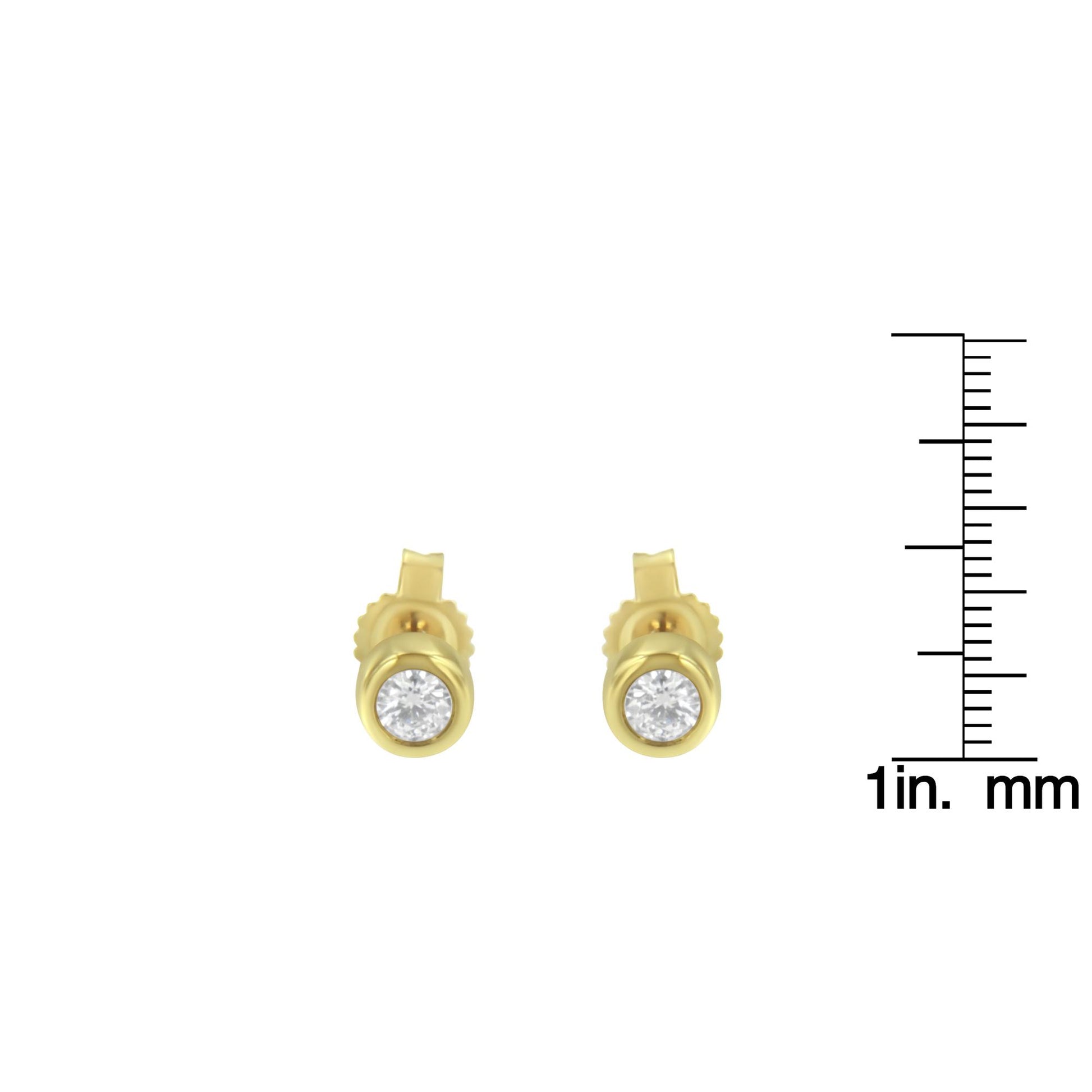 Front view of yellow metal stud earrings with round white gemstones in bezel settings, placed next to a ruler for size reference.