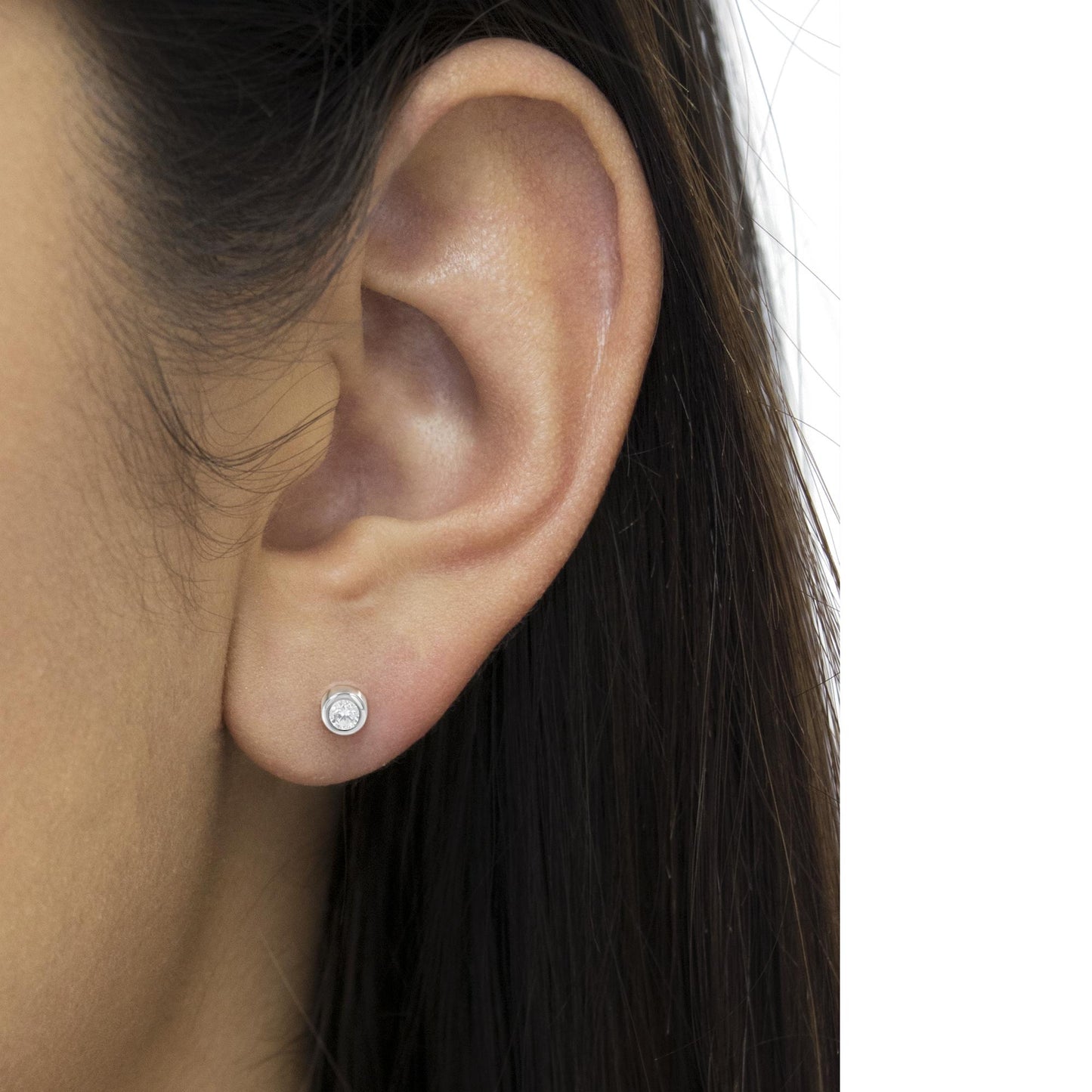 Close-up side view of a white metal round bezel-set white gemstone stud earring on a model's ear.