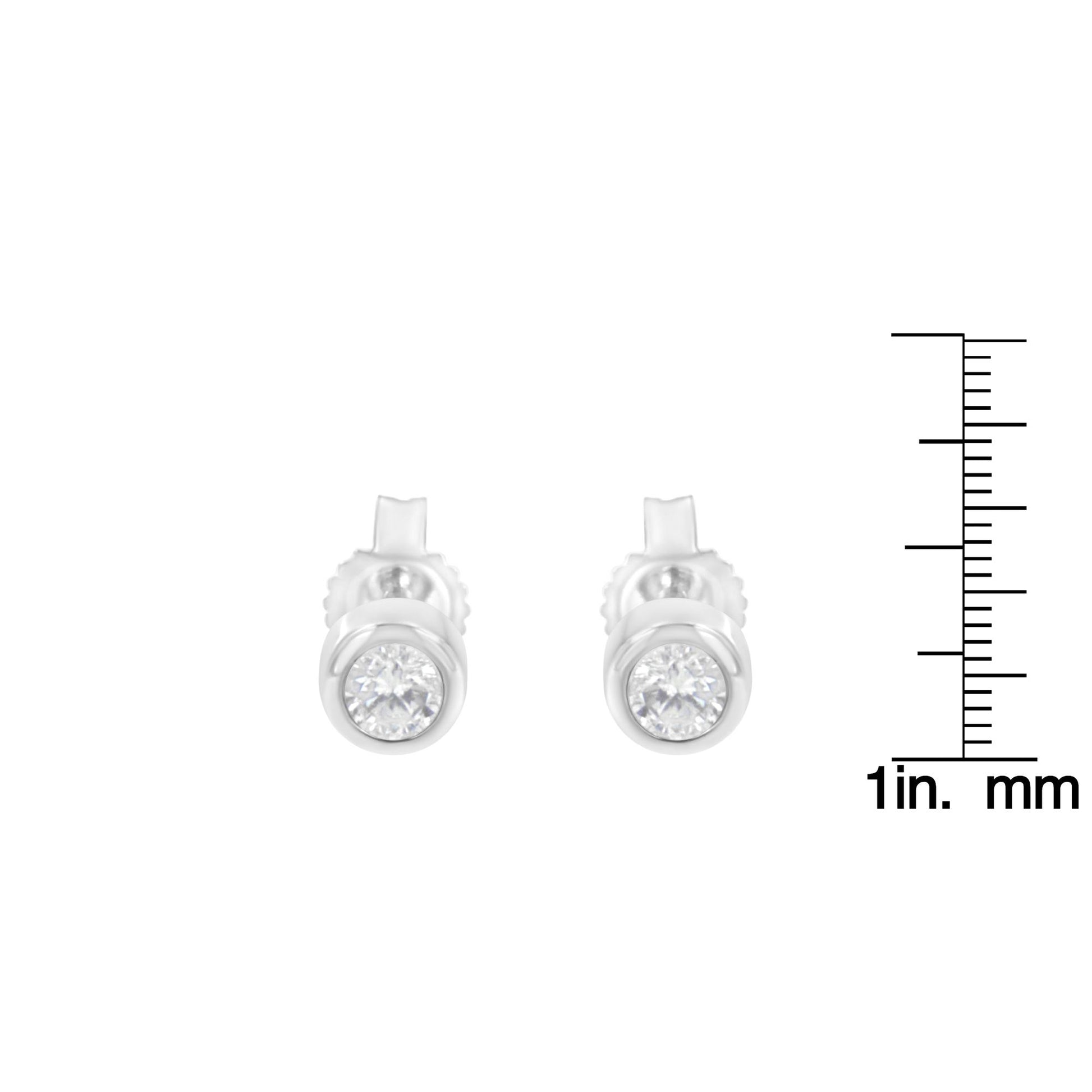 Pair of white metal stud earrings with round white gemstones in bezel setting, front view, placed next to a ruler for size reference.