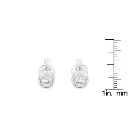 Pair of white metal stud earrings with round white gemstones in bezel setting, front view, placed next to a ruler for size reference.