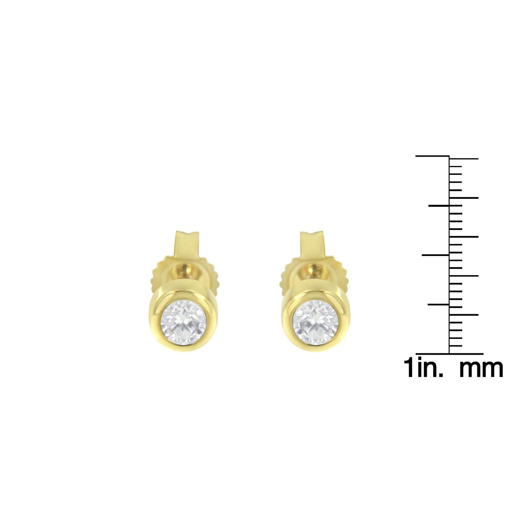 Front-facing shot of yellow metal stud earrings with round white gemstones in bezel settings, shown next to a ruler for size reference.