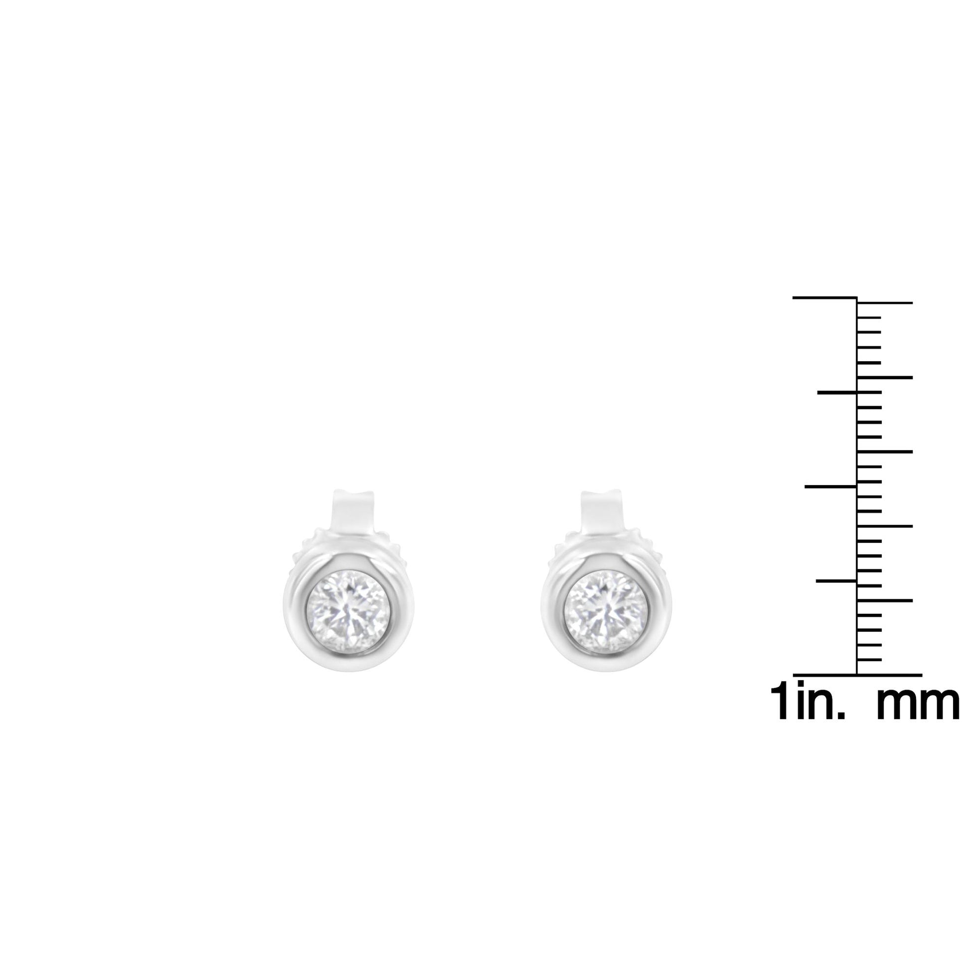 Front view of a pair of white metal earrings with round bezel-set white gemstones, shown next to a ruler for size reference.