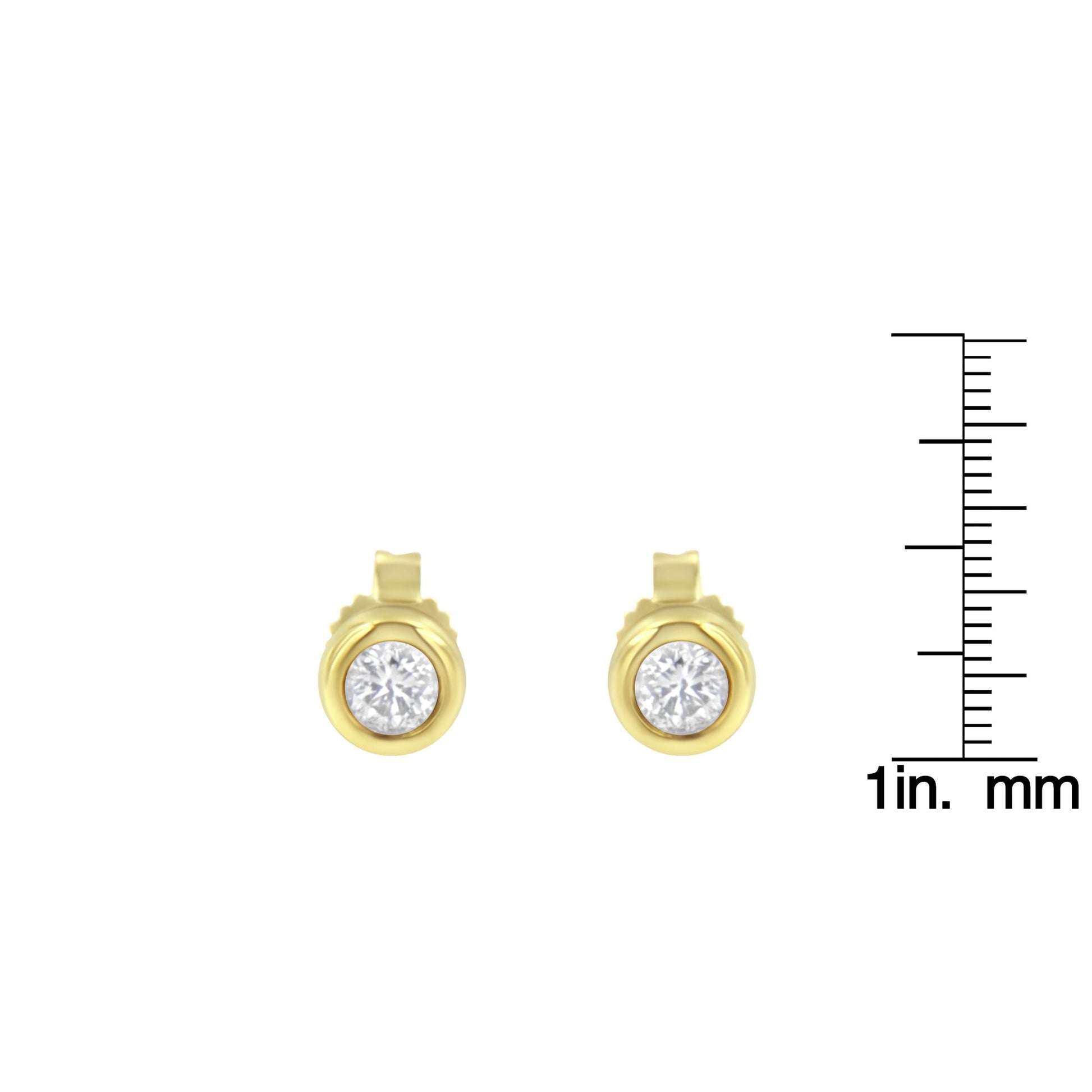 Front view of yellow metal stud earrings with round white gemstones in bezel settings, shown with a ruler for size reference.