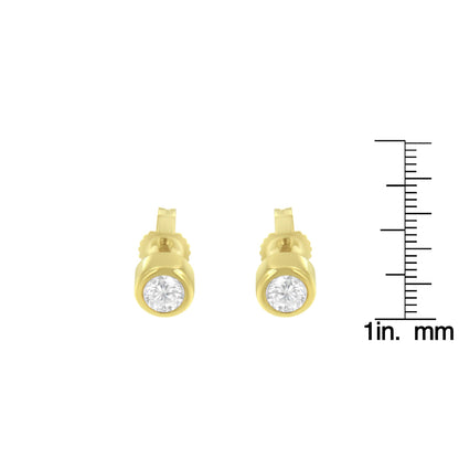Front-facing shot of round white gemstone bezel-set yellow metal stud earrings shown with a ruler for size reference.
