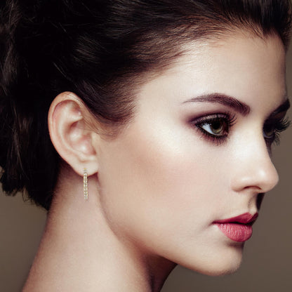 Close-up side profile of a model wearing yellow metal hoop earrings set with small round brownish gemstones in prong settings.