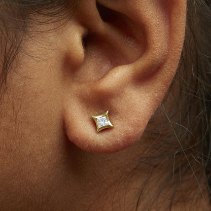 Close-up side view of an earlobe on a model wearing a yellow metal stud earring with a princess-shaped white gemstone set invisibly.